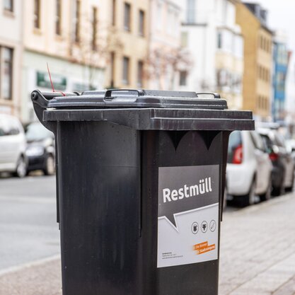 Eine schwarze Tonne auf der "Restmüll" steht. Im Hintergrund ist eine belebte Straße. | © Die Bremer Stadtreinigung