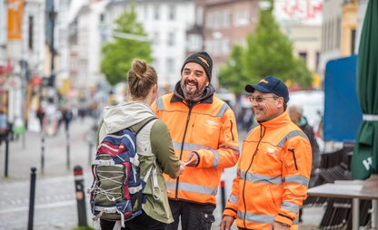 Zwei Angestellte von DBS beraten eine Bürgerin in einer belebten Straße. | © Die Bremer Stadtreinigung