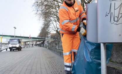 Ein Mitarbeiter von DBS leert an der Bremer Schlachte zwei öffentliche Abfallbehälter. Im Hintergrund ist das Entsorgungsfahrzeug an der Promenade zu sehen. | © Die Bremer Stadtreinigung